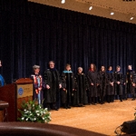 Members of faculty stand on stage while listening to remarks